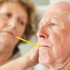 older adult man with thermometer in mouth being comforted by wife